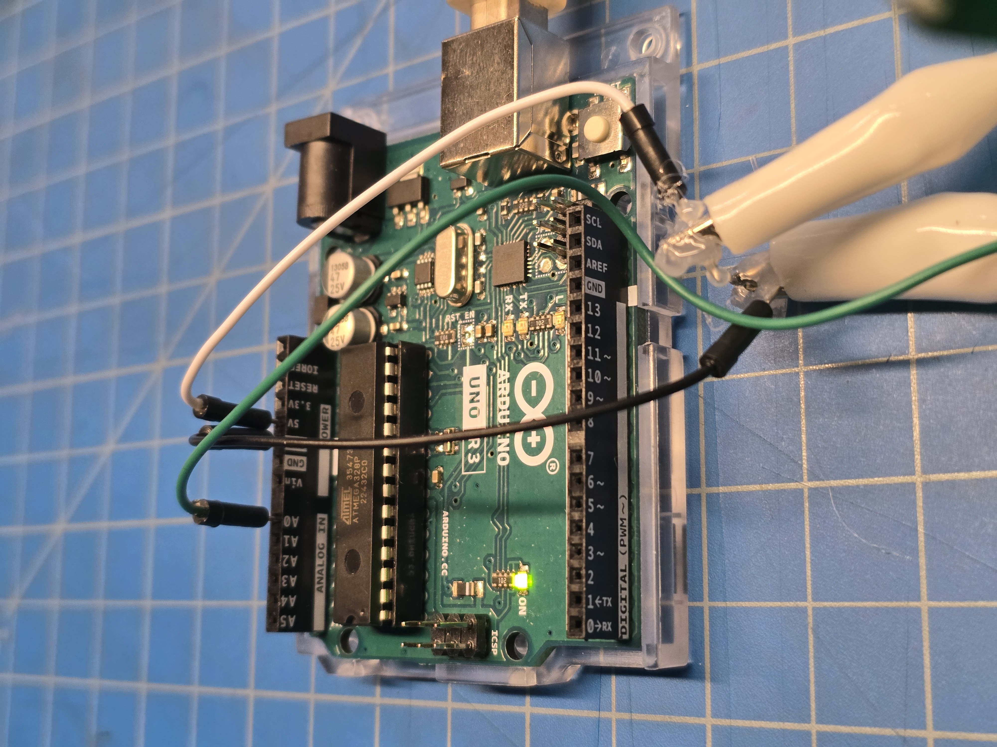 Close‑up of Arduino Uno: Hall‑sensor connector and alligator clip ends hot‑glued/insulated to prevent shorts when contacts touch